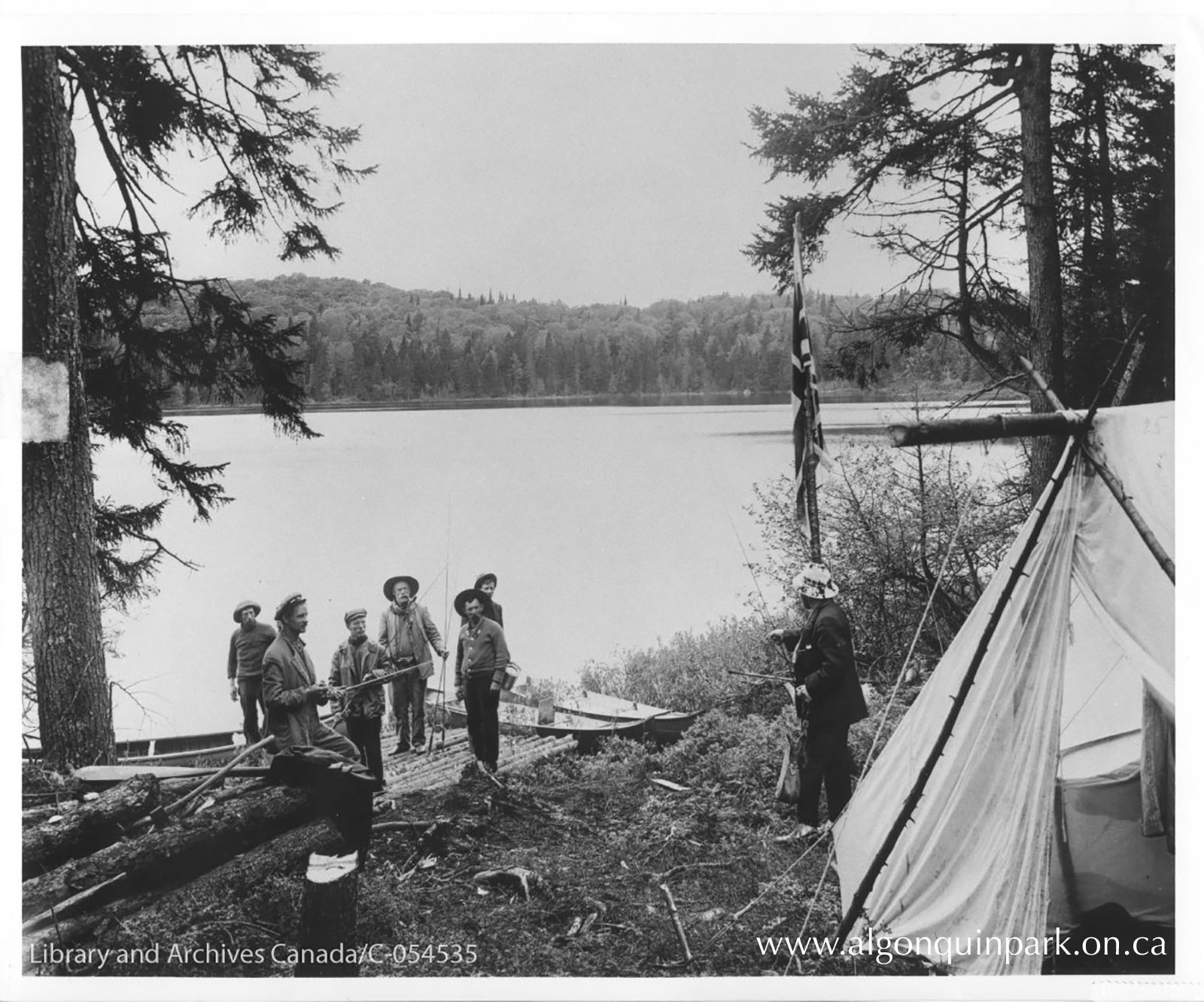 A fishing party stands on a landing by a lake. Fred Cook raises the Union Flag at their campsite. Library and Archives Canada/C-054535.